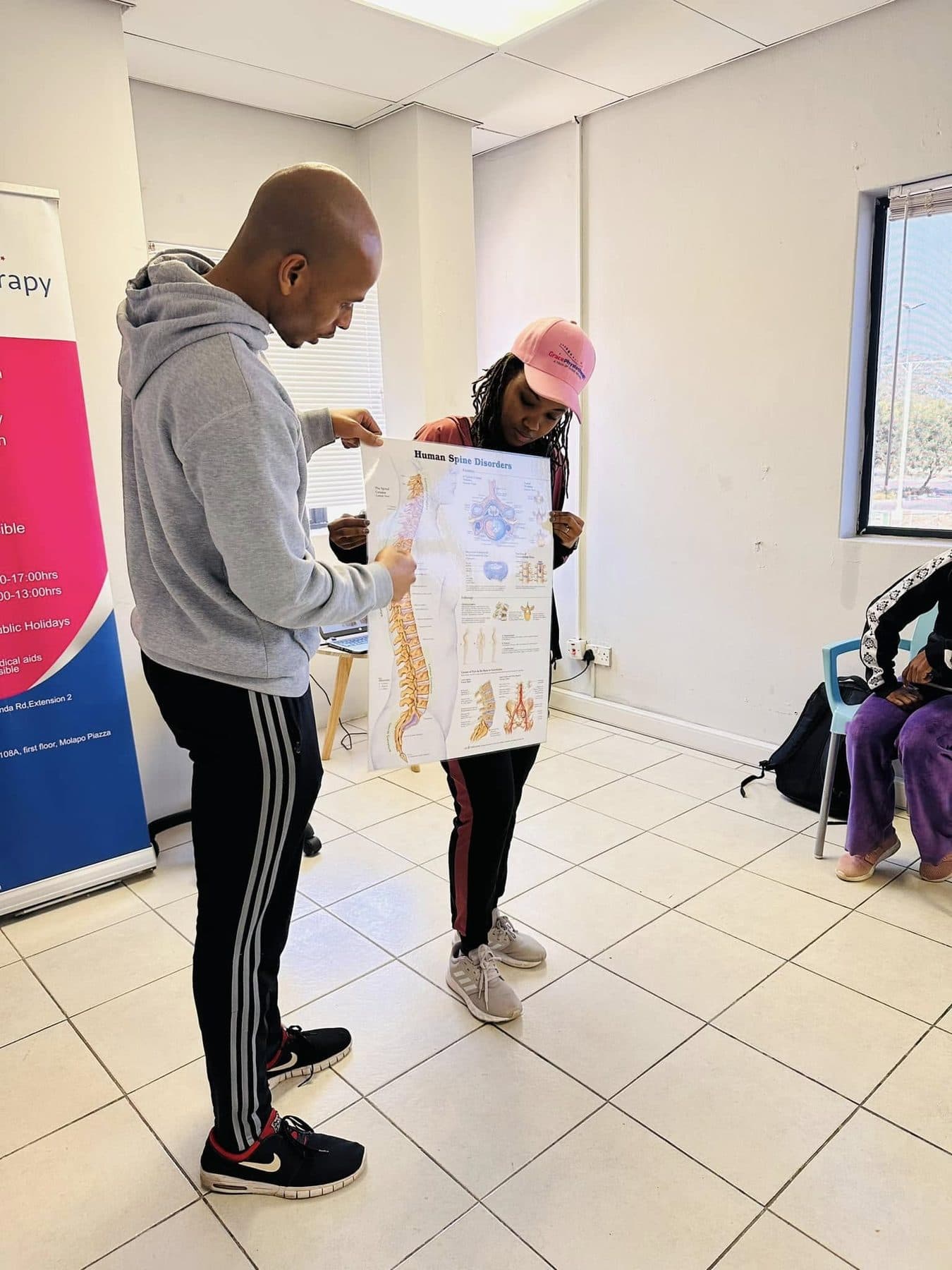 A Grace Physiotherapy therapist talking a patient through a spinal anatomy chart during assessment.