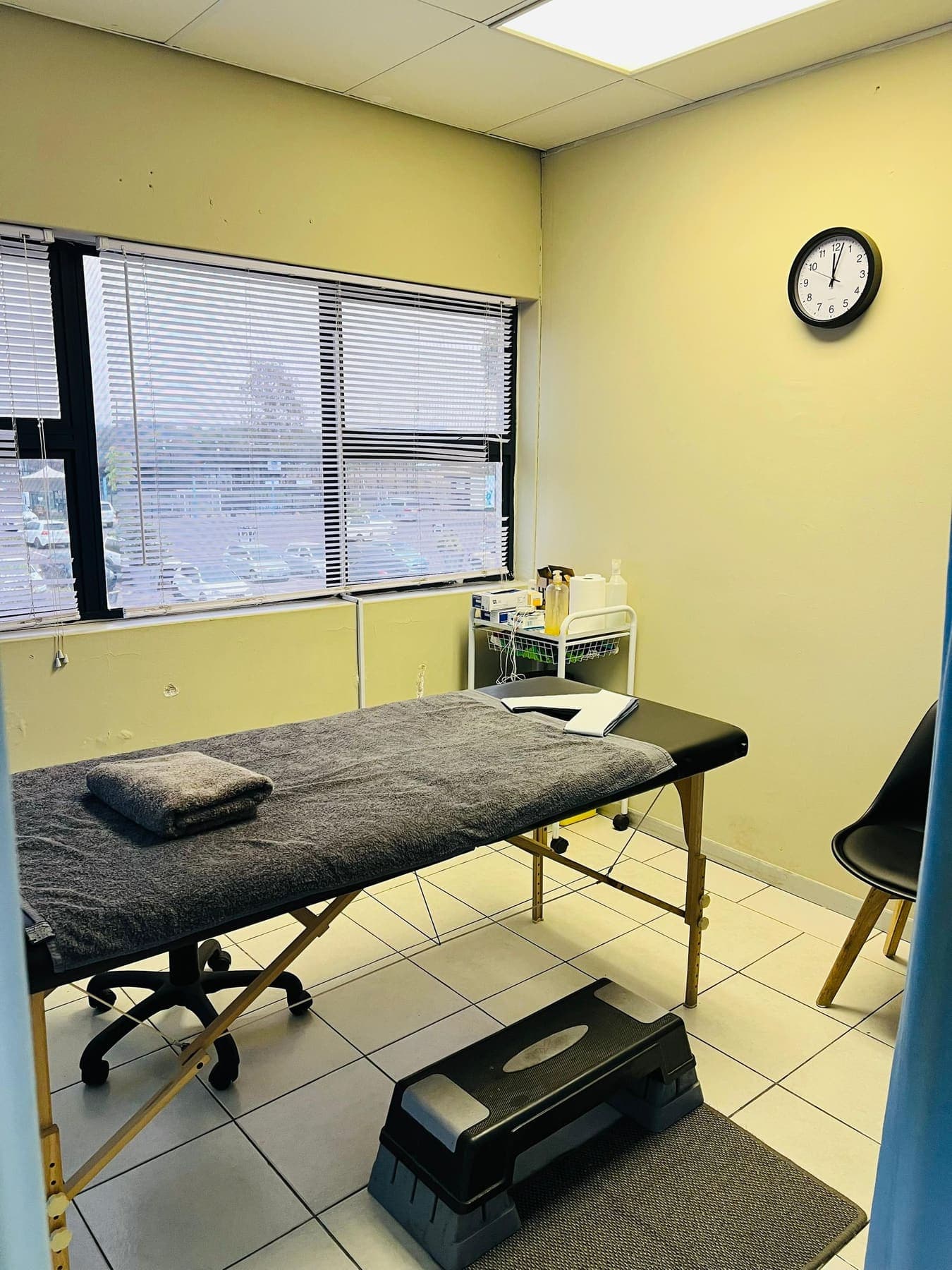 A Molapo Crossing treatment room with a plinth, adjustable stool, step platform and a window onto the car park.